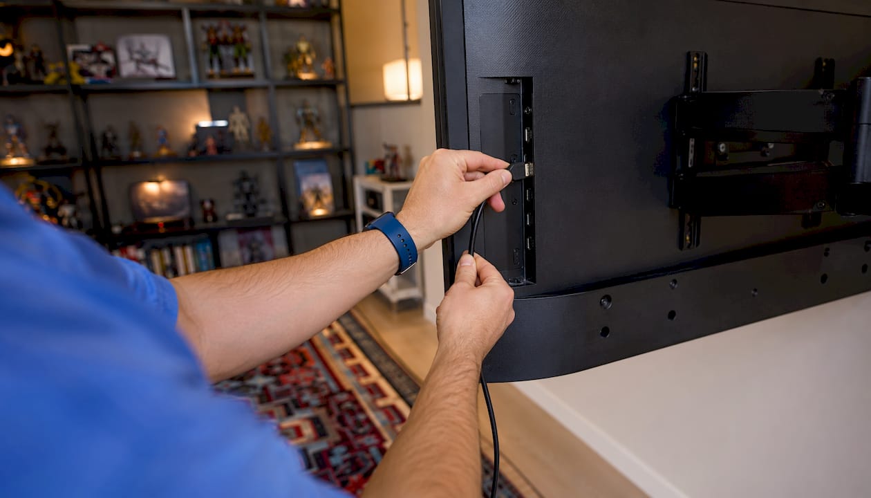 Hands plugging HDMI cable into TV port